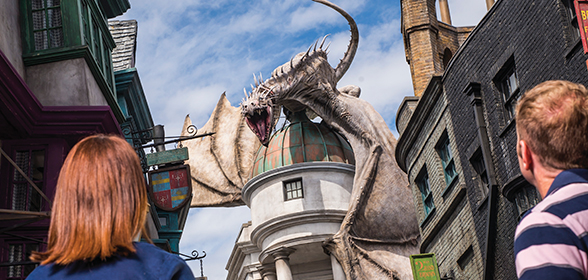 Pessoas caminham em direção a um dragão em cima de uma casa no The Wizarding World of Harry Potter - Diagon Alley™.