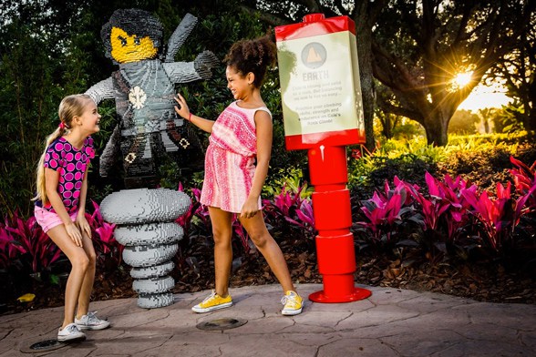 Duas meninas riem uma para a outra em frente a uma figura de ninja feita com blocos LEGO® no Ninjago World, no evento NINJAGO® Days do LEGOLAND® Florida Resort.