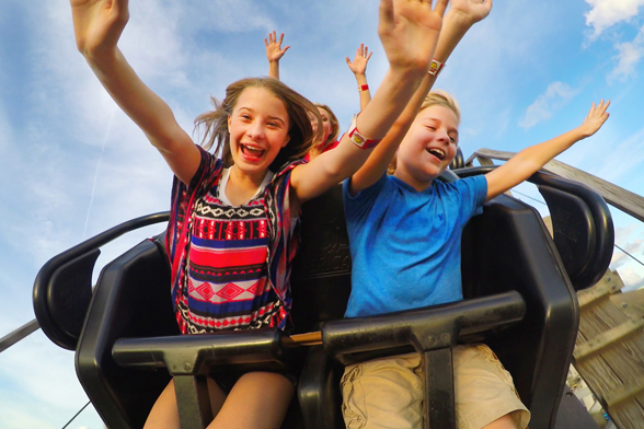 Duas crianças com os braços estendidos sorriem enquanto estão em uma montanha-russa no Fun Spot, em Orlando.