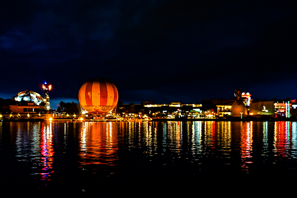 Imagem do Disney Springs à noite, com muitas luzes ao fundo refletidas em um lago.