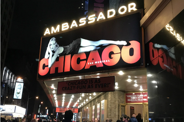 Ambassador Theater, teatro que abriga o show Chicago, na Broadway. Acima da entrada, vê-se um pôster com uma mulher deitada em cima da palavra "Chicago".