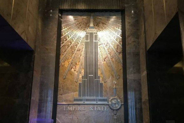 Representação do Empire State Building no lobby do prédio, em que há o desenho do arrnha-céu, com raios de luz saindo do seu mastro (Foto: Natália Grandi)