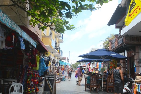 Rua de pedestres em Isla Mujeres durante o dia. Vê-se vendas de artesanatos e turistas passeando. Isla Mujeres é uma das paradas do Dancer Cruise em Cancun.