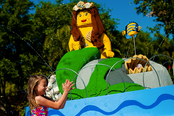 Uma menina brinca no LEGOLAND Water Park. Atrás dela, vê-se uma sereia feita com blocos LEGO®, durante o dia.