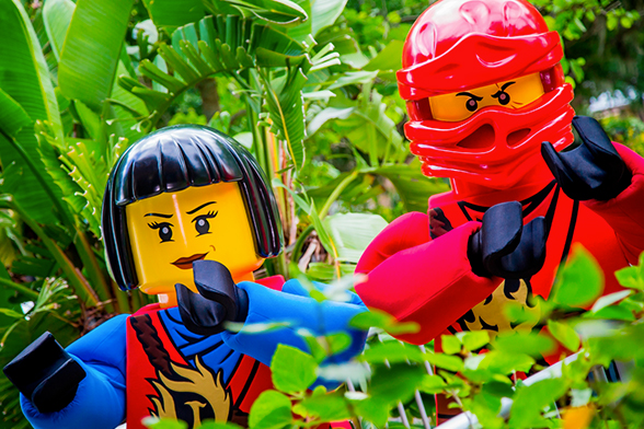 Dois personagens durante o evento LEGO® NINJAGO® Days. As figuras, feitas com blocos LEGO® em tamanho real, estão no LEGOLAND® Florida Resort, entre vários arbustos.